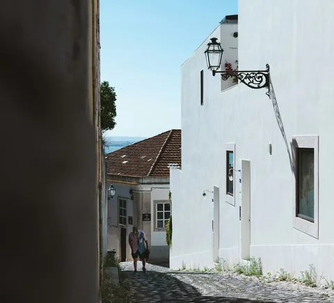 People walking down a narrow whitewashed Alfama cobblestone lane.