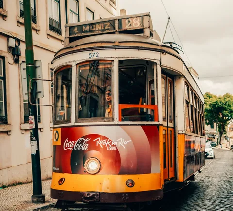 Historic yellow-and-red Tram 28 on a cobblestone Lisbon street.
