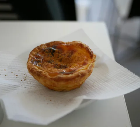 Authentic Portuguese pastel de nata on café paper beside coffee.