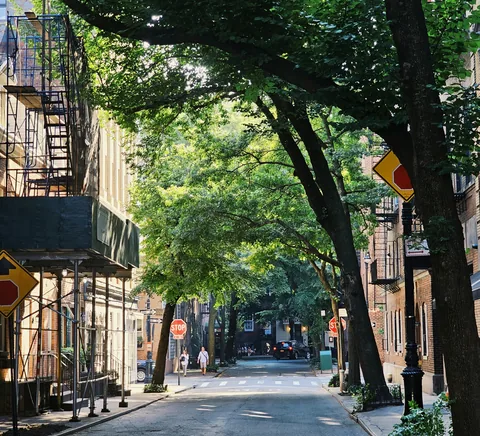 Leafy Greenwich Village residential street with brownstones and fire escapes, July 2023.