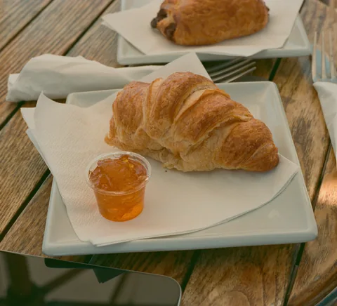 Real croissant and jam photographed at a Paris cafe, confirmed by source description. Natural film colour, authentic table detail; no venue endorsement or claim that this single food captures every Paris meal.
