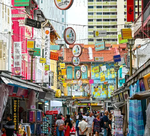 Busy pedestrian shopping lane with shophouses, signs and people in Singapore Chinatown.