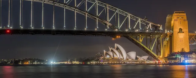 Sydney Opera House beneath Harbour Bridge, night-time view from Blues Point Reserve.