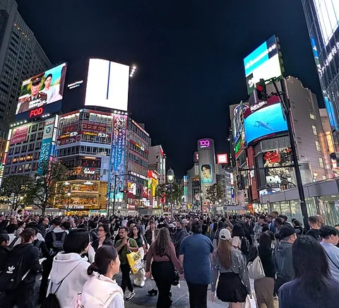 People crossing in Shibuya amid illuminated urban signage.